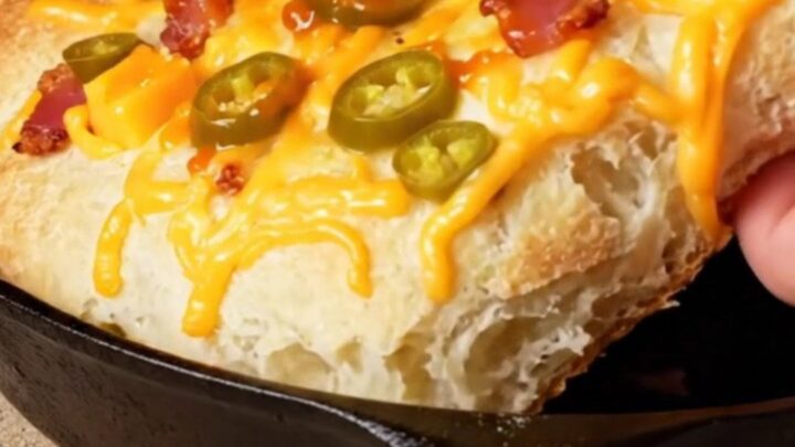 Extreme close-up of a golden brown jalapeño cheddar and bacon focaccia with visible lacy cheese edges in a cast-iron pan.