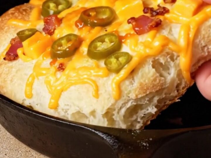Extreme close-up of a golden brown jalapeño cheddar and bacon focaccia with visible lacy cheese edges in a cast-iron pan.