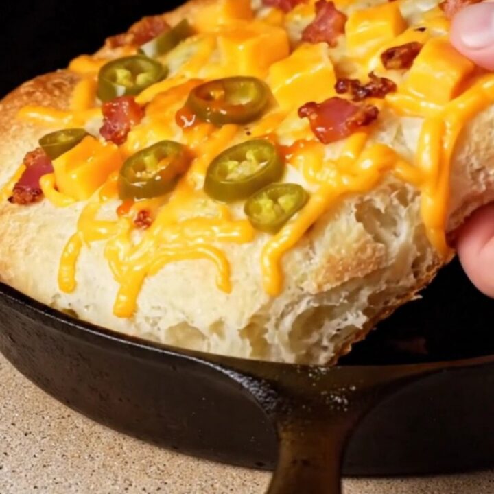 Extreme close-up of a golden brown jalapeño cheddar and bacon focaccia with visible lacy cheese edges in a cast-iron pan.