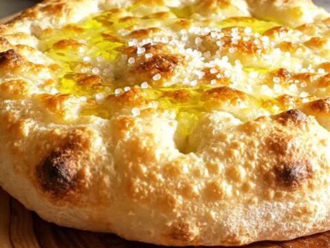 A close-up of a crispy, golden-brown Focaccia di Recco being torn open to reveal molten stracchino cheese.