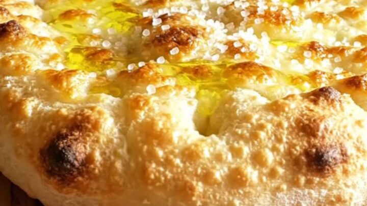 A close-up of a crispy, golden-brown Focaccia di Recco being torn open to reveal molten stracchino cheese.