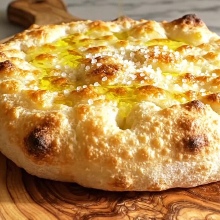 A close-up of a crispy, golden-brown Focaccia di Recco being torn open to reveal molten stracchino cheese.