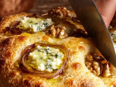 A golden-brown focaccia topped with caramelized onions, gorgonzola, and walnuts, drizzled with honey.