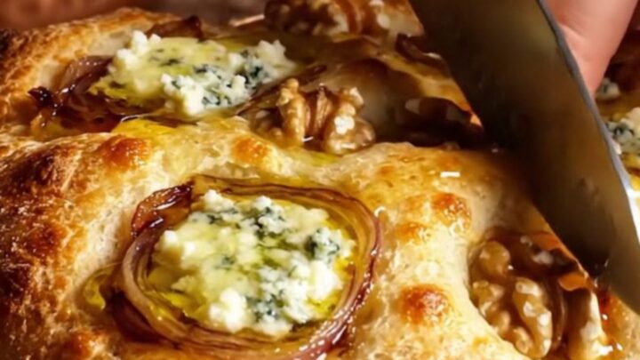 A golden-brown focaccia topped with caramelized onions, gorgonzola, and walnuts, drizzled with honey.