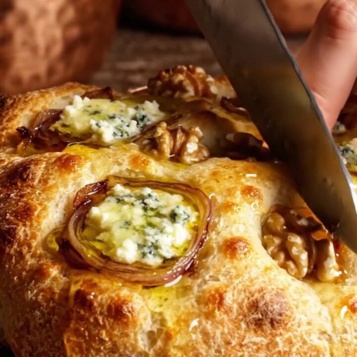 A golden-brown focaccia topped with caramelized onions, gorgonzola, and walnuts, drizzled with honey.