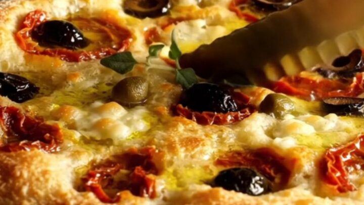 A crispy Pugliese Focaccia Barese with charred tomatoes and olives in a cast iron pan.
