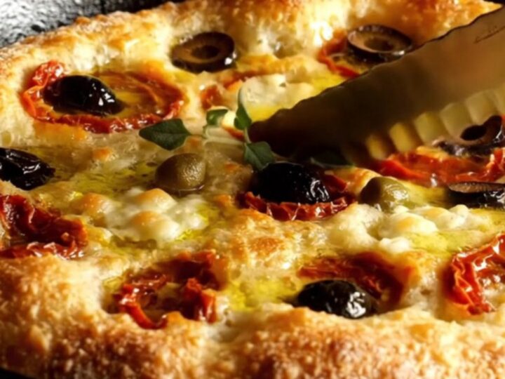 A crispy Pugliese Focaccia Barese with charred tomatoes and olives in a cast iron pan.