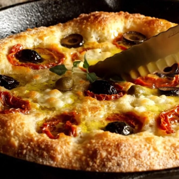 A crispy Pugliese Focaccia Barese with charred tomatoes and olives in a cast iron pan.