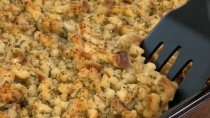 A close-up shot of a scoop of golden herb stuffing casserole being lifted, revealing creamy shredded chicken underneath.
