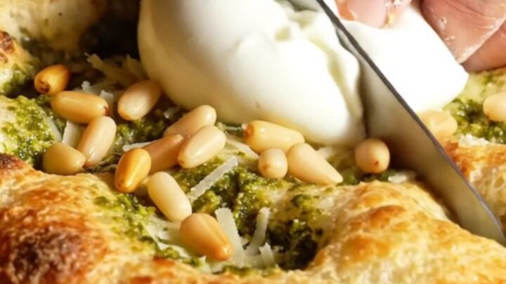A golden, crispy focaccia bread topped with swirls of green basil pesto and creamy burrata cheese.