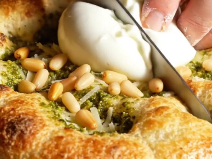 A golden, crispy focaccia bread topped with swirls of green basil pesto and creamy burrata cheese.
