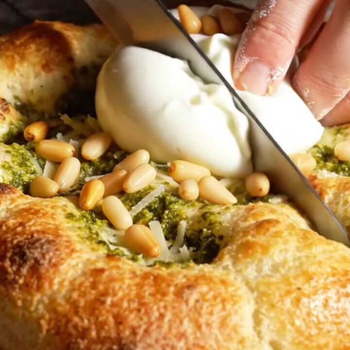 A golden, crispy focaccia bread topped with swirls of green basil pesto and creamy burrata cheese.