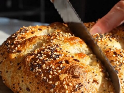A warm, golden-brown everything bagel focaccia with visible pockets of scallion cream cheese, displayed on a marble surface.