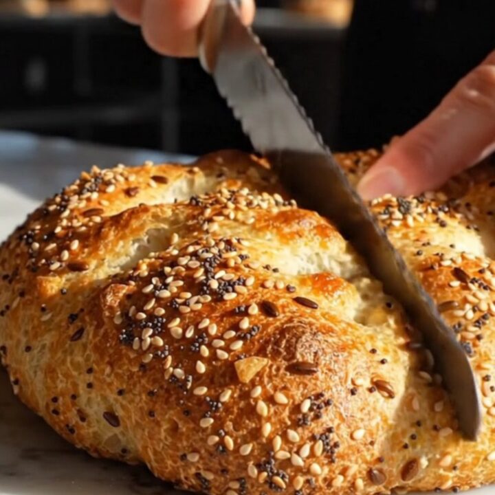A warm, golden-brown everything bagel focaccia with visible pockets of scallion cream cheese, displayed on a marble surface.