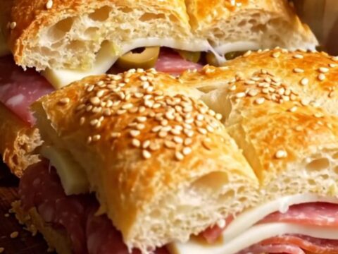 A sliced muffuletta focaccia slab showing layers of Italian meats and provolone cheese.