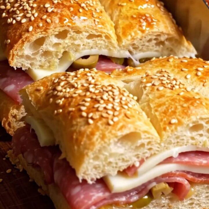 A sliced muffuletta focaccia slab showing layers of Italian meats and provolone cheese.