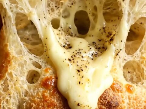 A close-up of a golden, crispy focaccia bread topped with melted Pecorino Romano and cracked black pepper.