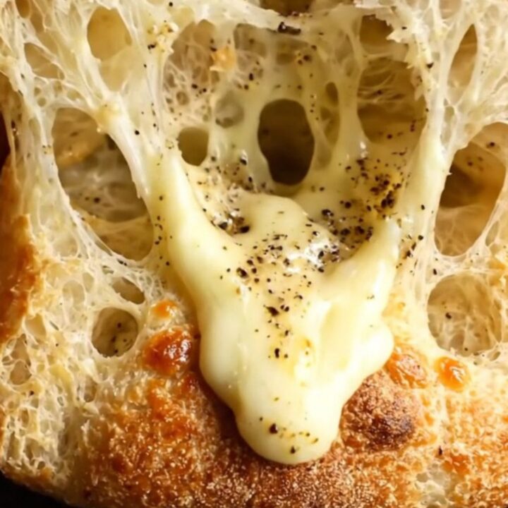 A close-up of a golden, crispy focaccia bread topped with melted Pecorino Romano and cracked black pepper.