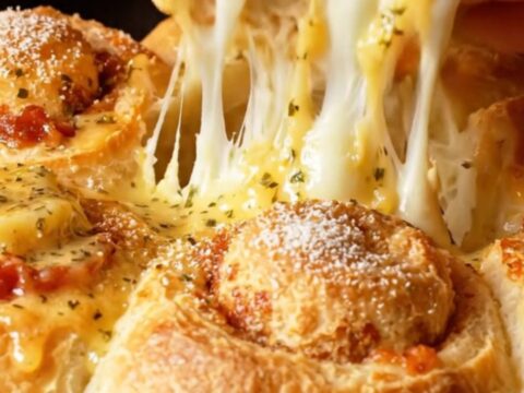 A close-up of golden brown pepperoni focaccia rolls in a skillet with melting mozzarella cheese strings.