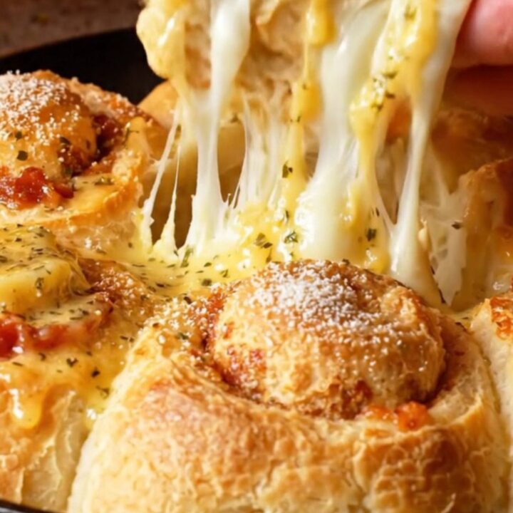 A close-up of golden brown pepperoni focaccia rolls in a skillet with melting mozzarella cheese strings.