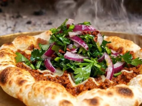 A crispy, rolled-up Turkish lahmacun filled with fresh parsley and red onions with a lemon wedge nearby.