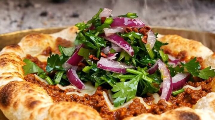 A crispy, rolled-up Turkish lahmacun filled with fresh parsley and red onions with a lemon wedge nearby.