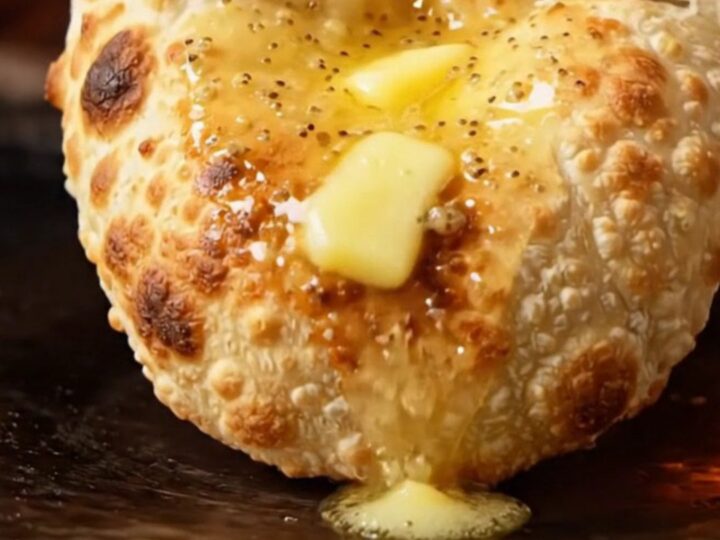 A close-up shot of a stuffed garlic cheese naan being torn open, revealing melted cheese and fresh cilantro.