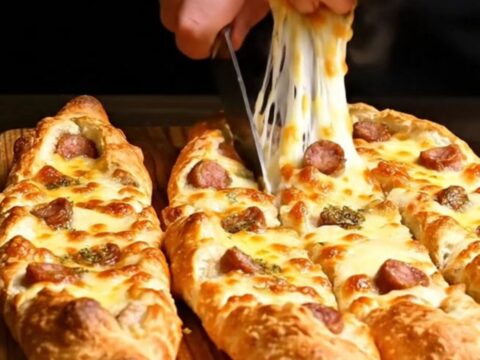 A close-up of a golden brown Turkish pide boat filled with melted cheese and spicy sujuk sausage.