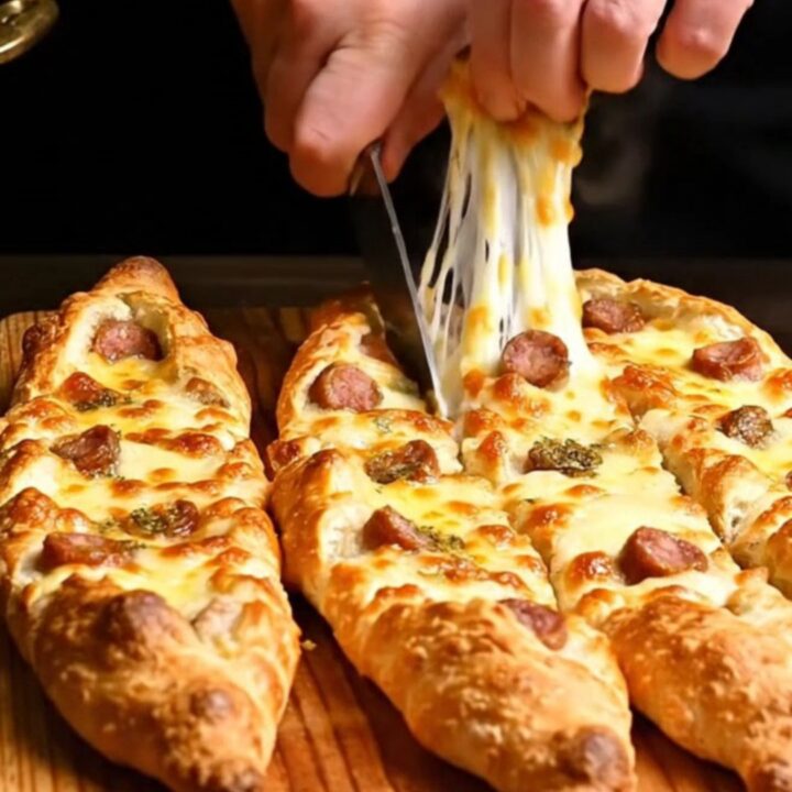 A close-up of a golden brown Turkish pide boat filled with melted cheese and spicy sujuk sausage.