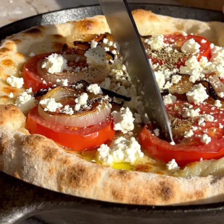 A rustic Greek Ladenia flatbread with tomatoes, onions, and feta on a wooden table.
