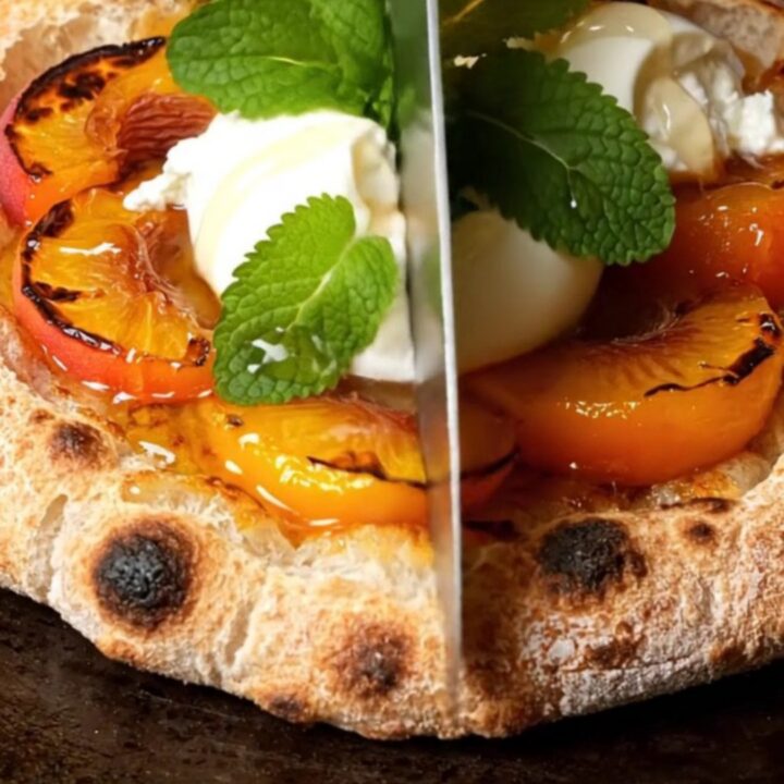 A close-up of a grilled sourdough flatbread topped with charred peach wedges and creamy burrata cheese.