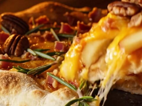 A close-up of a smoked gouda and apple flatbread with melted cheese stretching over thin apple slices.