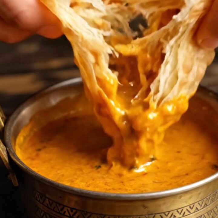 A stack of freshly cooked, golden-brown Malabar parottas with visible flaky layers.