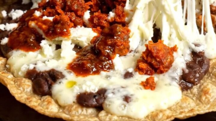 A crispy, golden Oaxacan Tlayuda topped with refried beans, chorizo, melted string cheese, avocado, and salsa roja.