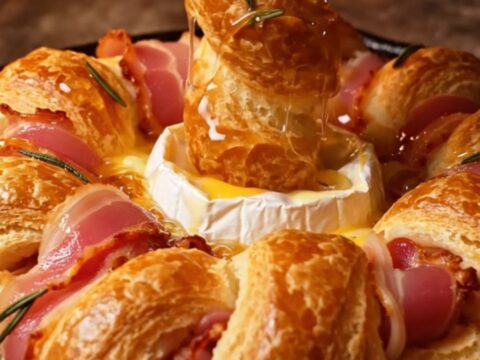 A golden, circular puff pastry wreath filled with a baked Camembert wheel and wrapped in crispy bacon strips.