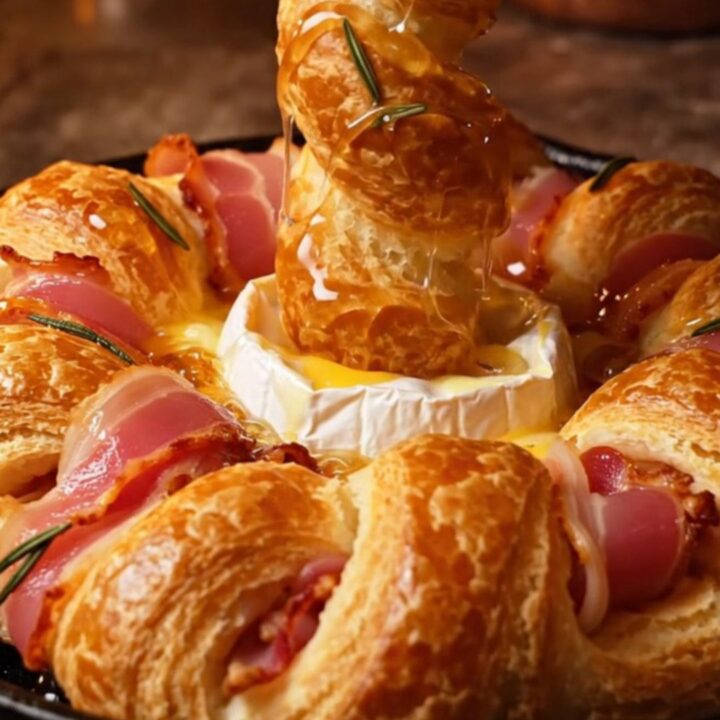 A golden, circular puff pastry wreath filled with a baked Camembert wheel and wrapped in crispy bacon strips.