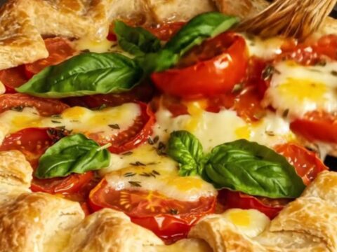 A rustic heirloom tomato and Boursin cheese galette with a golden cheddar crust sitting on a wooden surface.