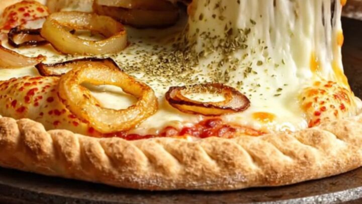A giant, golden-brown fugazzeta empanada pie cut into wedges, showing a massive pull of melted mozzarella and sweet onions.