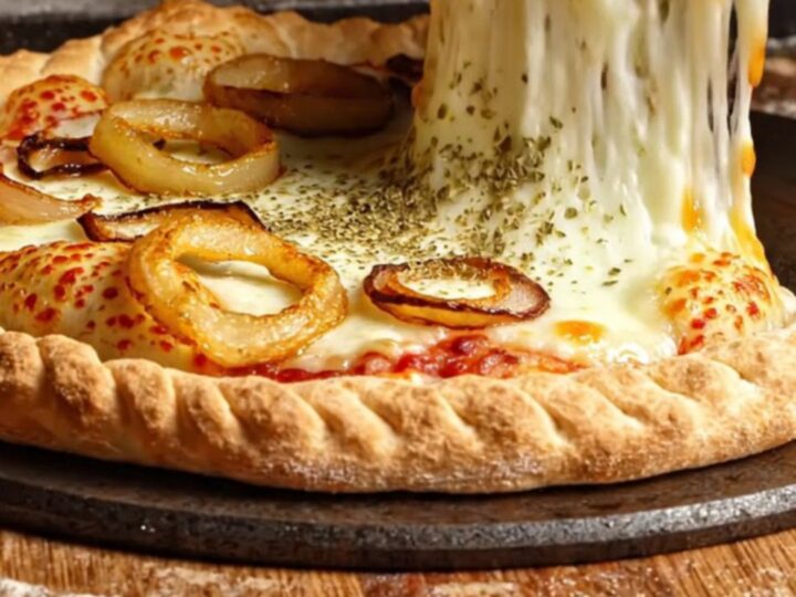 A giant, golden-brown fugazzeta empanada pie cut into wedges, showing a massive pull of melted mozzarella and sweet onions.