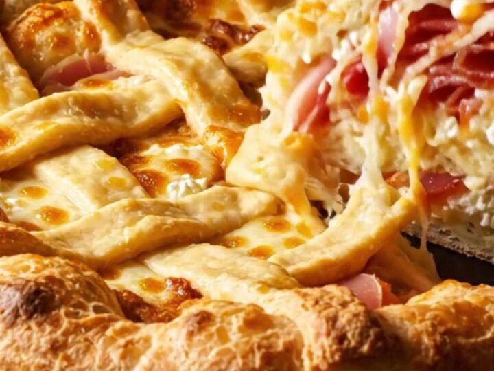 A tall, golden-brown Pizza Rustica pie with a lattice crust, sliced to reveal layers of ricotta, meat, and cheese.