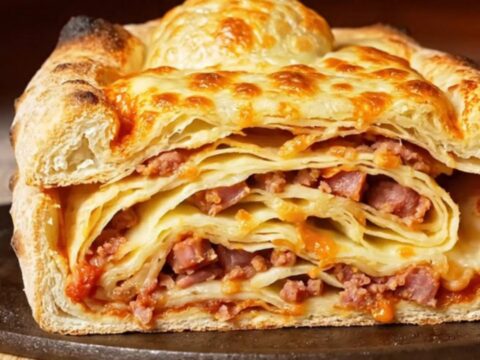 A close-up of a golden-brown Sicilian Scaccia sliced to reveal distinct, delicious layers of sausage and cheese.