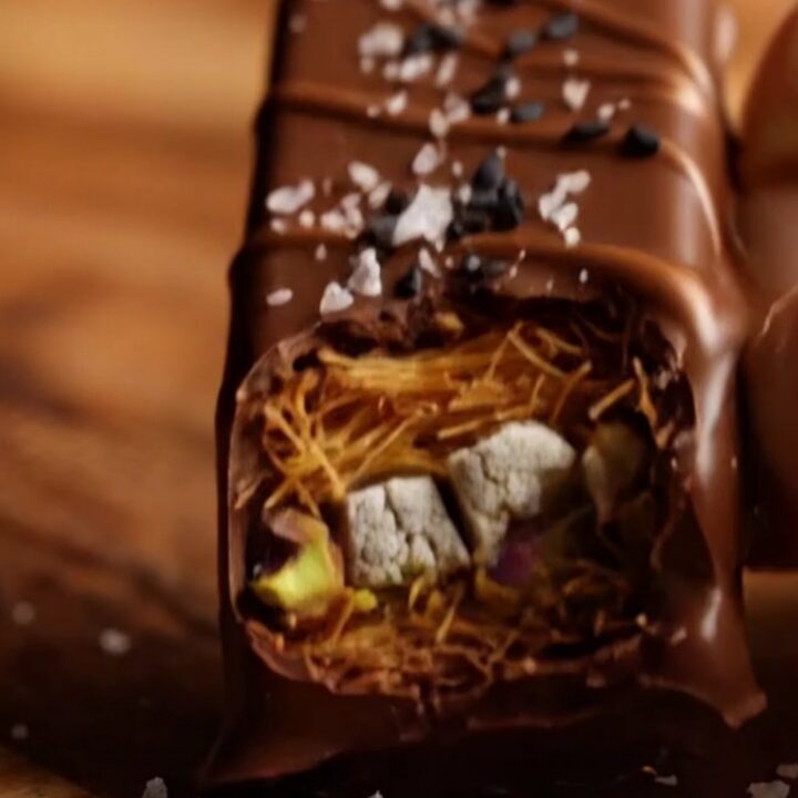 A close-up of a dark chocolate bar broken in half, revealing a crunchy golden kataifi and halva filling.