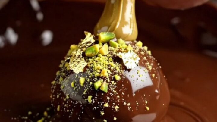 A close-up of a dark chocolate truffle split in half, showing a bright green pistachio and kataifi center.