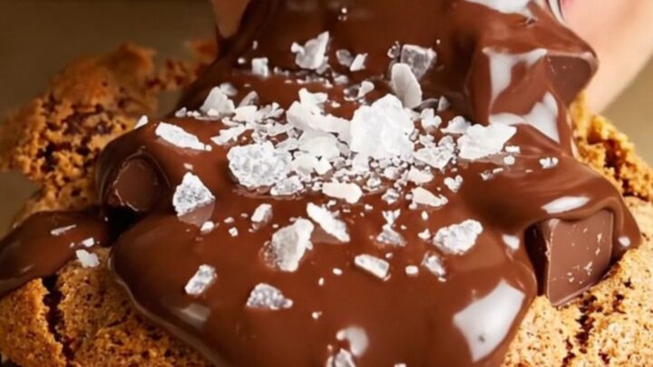 A close-up of a massive, six-ounce golden-brown cookie being pulled apart to reveal a molten chocolate core.