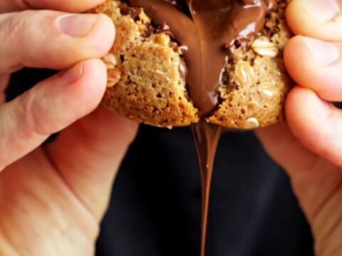 Extreme close-up of a warm monster cookie being pulled apart to reveal a molten peanut butter cup center.