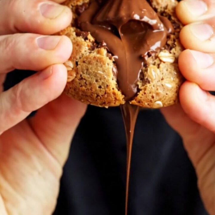Extreme close-up of a warm monster cookie being pulled apart to reveal a molten peanut butter cup center.
