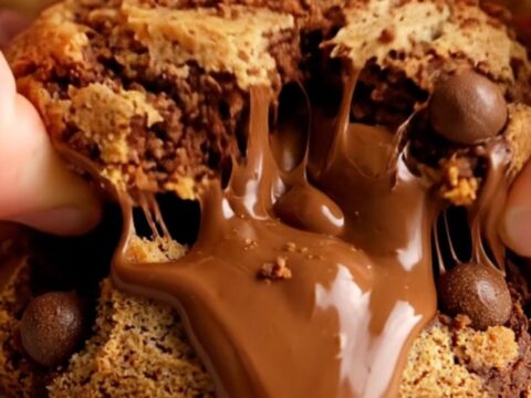 A close-up shot of a chewy cookie being pulled apart, revealing ribbons of melted fudge and pieces of malted milk balls.