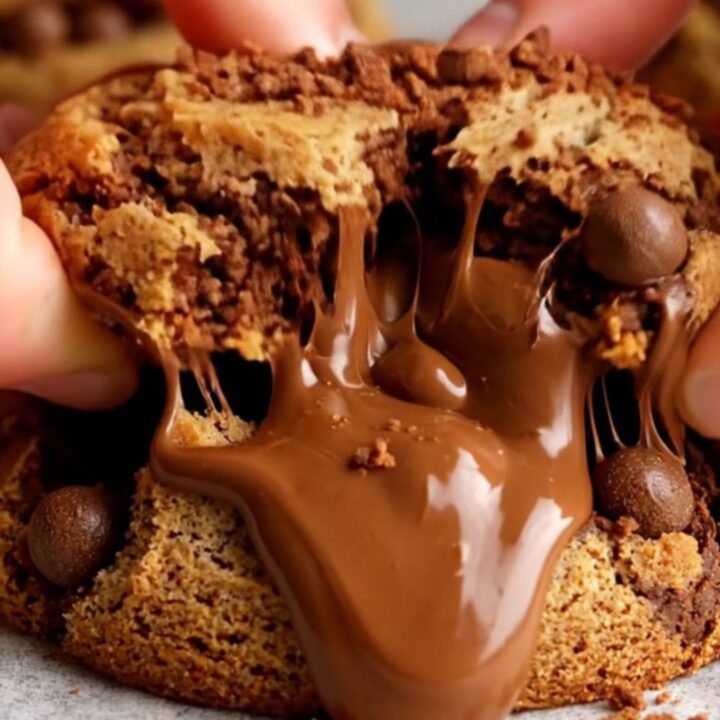 A close-up shot of a chewy cookie being pulled apart, revealing ribbons of melted fudge and pieces of malted milk balls.