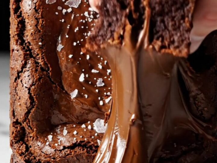 A close-up shot of a square of dark chocolate brownie being lifted with a spatula, revealing a glossy crinkle top.
