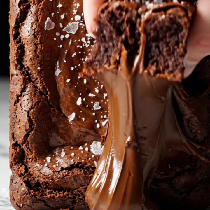 A close-up shot of a square of dark chocolate brownie being lifted with a spatula, revealing a glossy crinkle top.